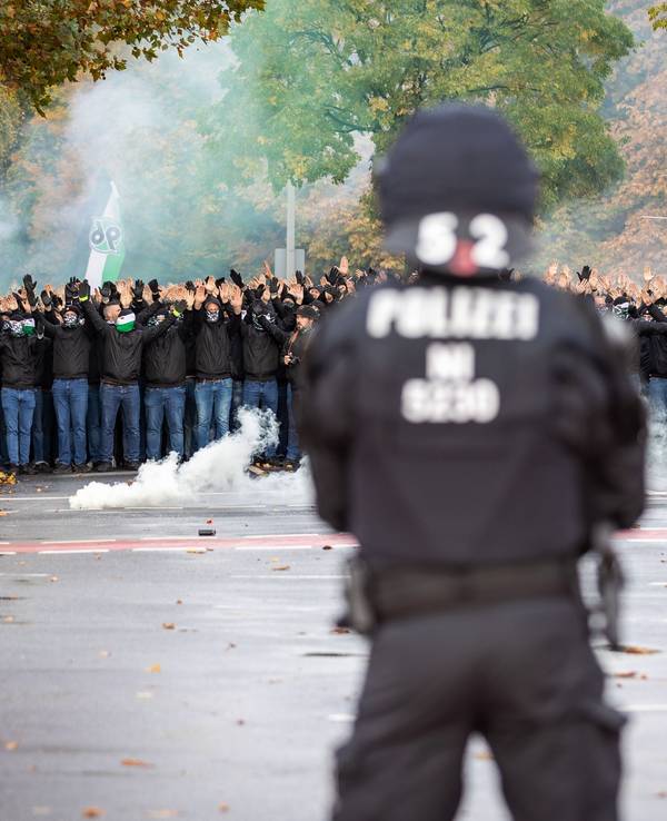 Ein Polizist der vor vielen vermummten Hannover 96 Fans steht.
