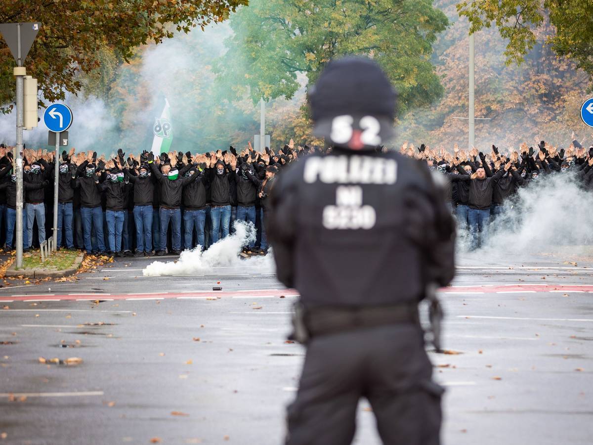 Ein Polizist der vor vielen vermummten Hannover 96 Fans steht.