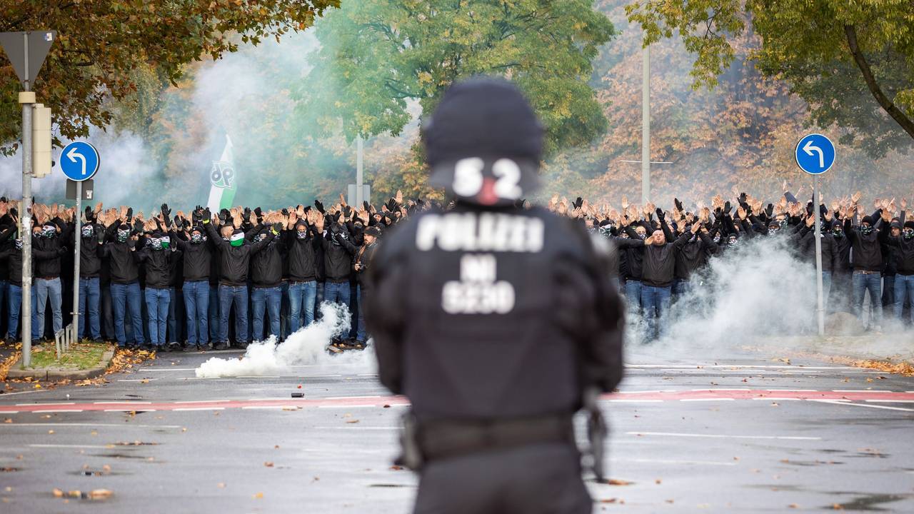 Ein Polizist der vor vielen vermummten Hannover 96 Fans steht.