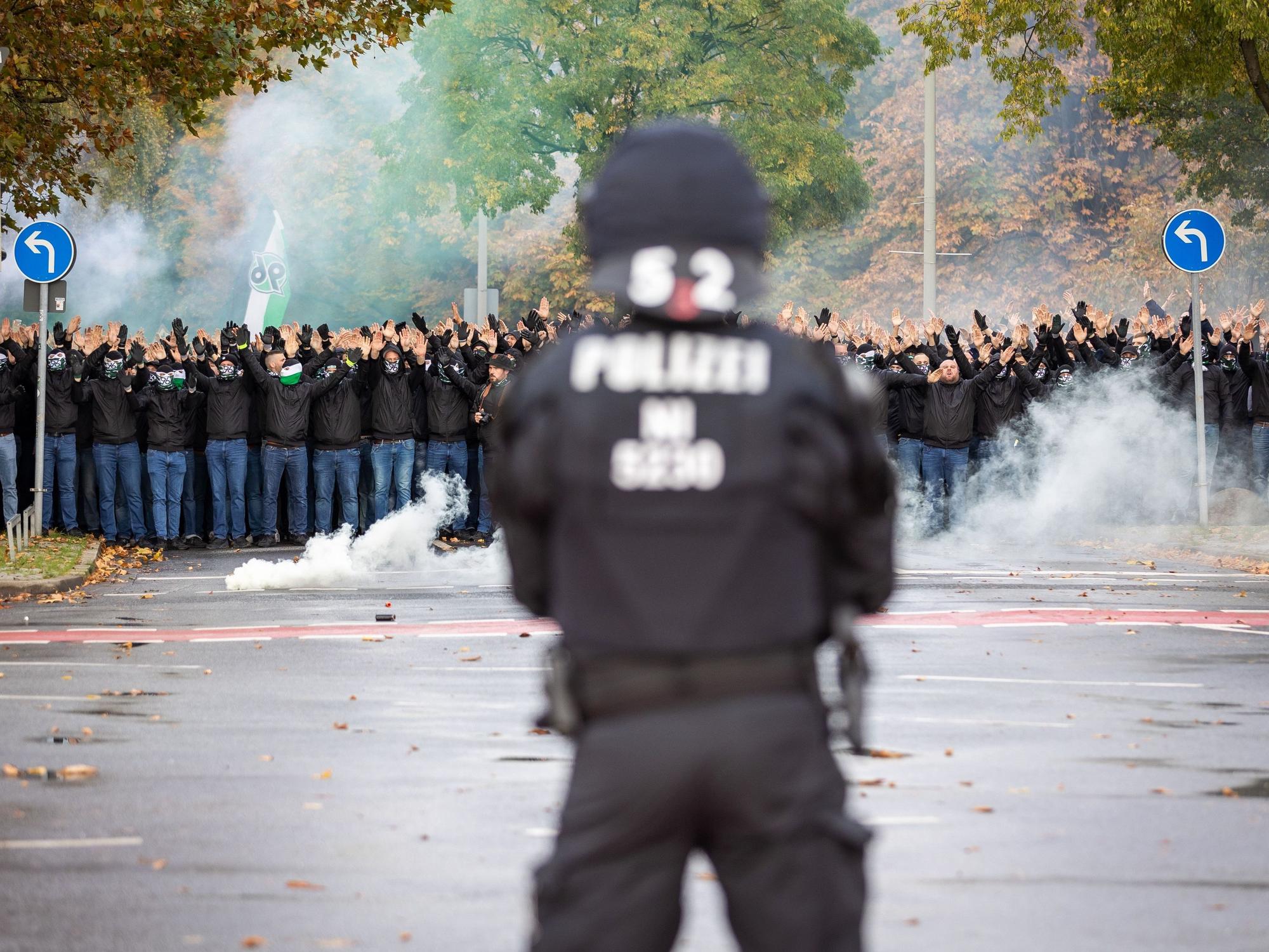 Ein Polizist der vor vielen vermummten Hannover 96 Fans steht.