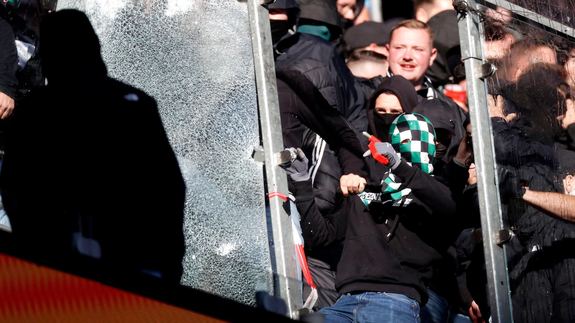Gladbach-Fans zertrümmern eine Glasscheibe mit einem Nothammer.
