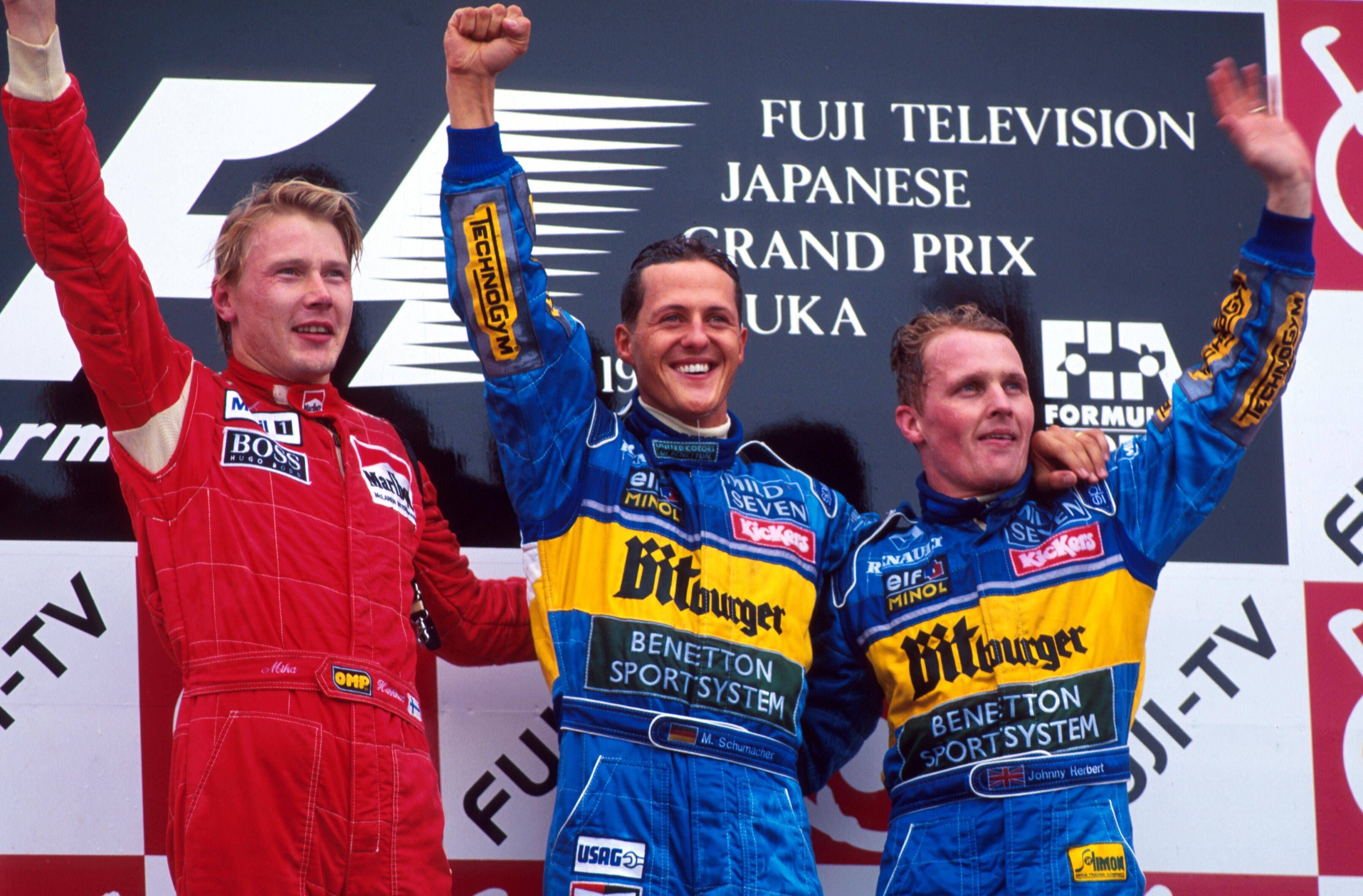 Mika Häkkinen, Michael Schumacher und Johnny Herbert stehen nebeneinander auf dem Podest und winken.