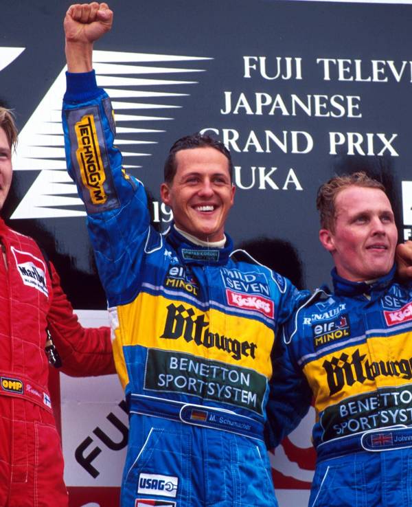 Mika Häkkinen, Michael Schumacher und Johnny Herbert stehen nebeneinander auf dem Podest und winken.