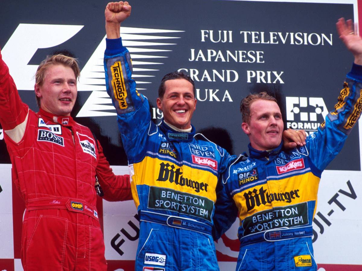 Mika Häkkinen, Michael Schumacher und Johnny Herbert stehen nebeneinander auf dem Podest und winken.