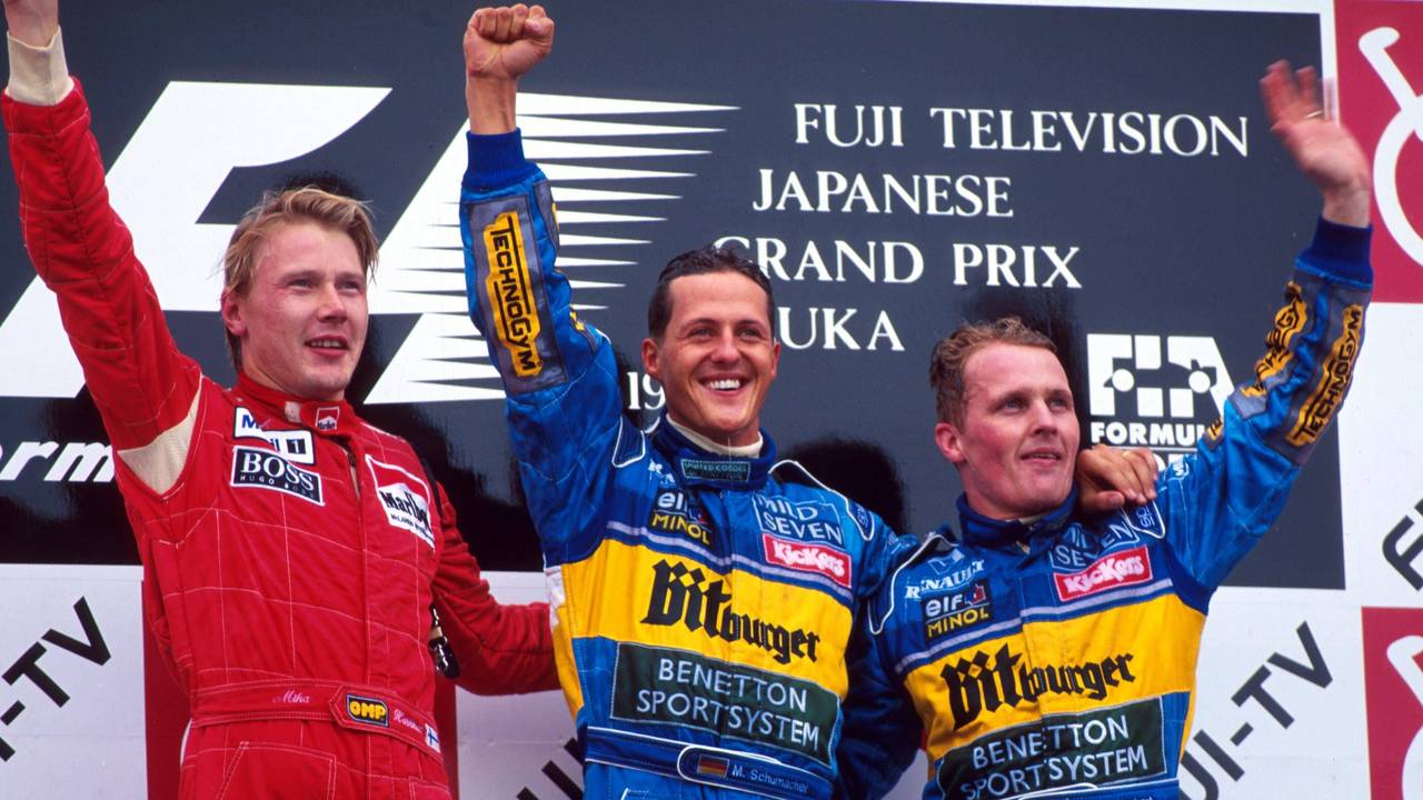 Mika Häkkinen, Michael Schumacher und Johnny Herbert stehen nebeneinander auf dem Podest und winken.