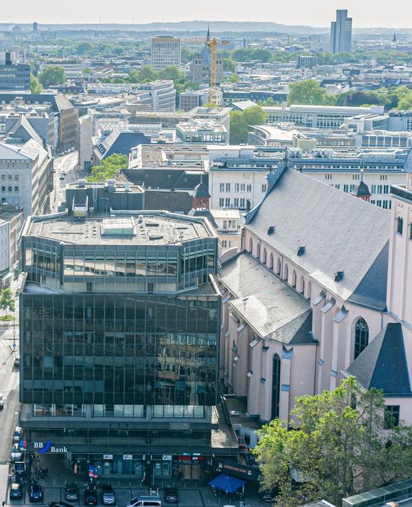 Ein dunkler, mehrstöckiger Klotz mit Glasfassade steht zwischen historischen Gebäuden.