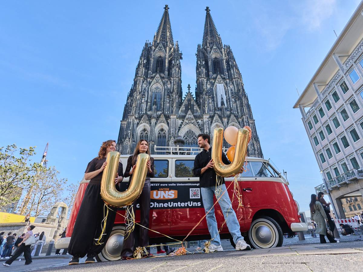 16.10.2026, Nordrhein-Westfalen, Köln: Milos Vukovic (r), Marie Zielcke (l) und Tabea Heynig, Schauspieler der RTL Daily Soap „Unter Uns“, stehen mit einem alten VW Bulli vor dem Dom. Die Schauspieler wollen für eine Fortführung der Serie werben, die RTL nach mehr als drei Jahrzehnten aus dem Programm nehmen wird. Foto: Rolf Vennenbernd/dpa +++ dpa-Bildfunk +++
