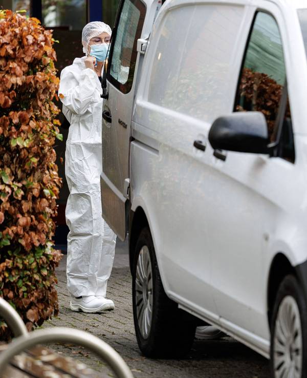 Eine Frau im Schutzanzug und mit Schutzmaske steht hinter einem Transporter.