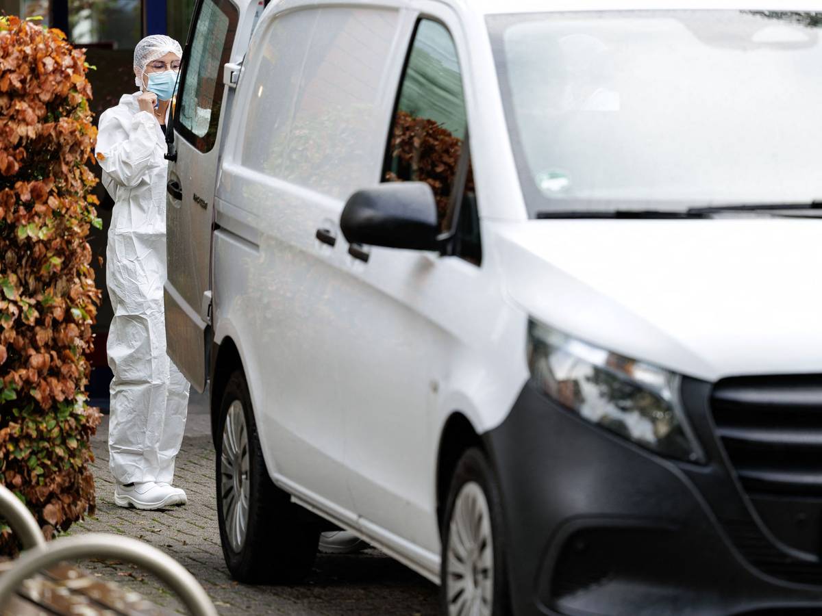Eine Frau im Schutzanzug und mit Schutzmaske steht hinter einem Transporter.