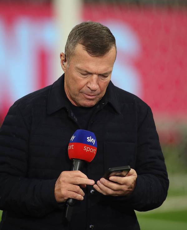 Lothar Matthäus guckt in sein Handy. In der anderen Hand hält er ein Sky-Mikrofon.