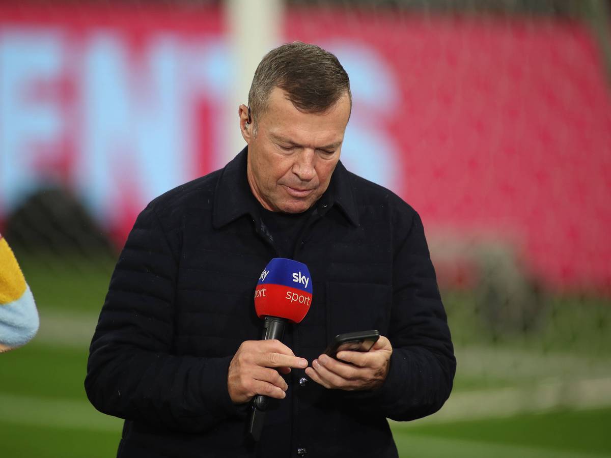 Lothar Matthäus guckt in sein Handy. In der anderen Hand hält er ein Sky-Mikrofon.