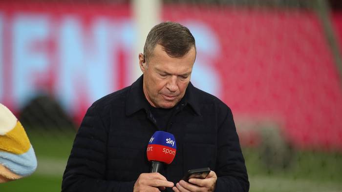 Lothar Matthäus guckt in sein Handy. In der anderen Hand hält er ein Sky-Mikrofon.