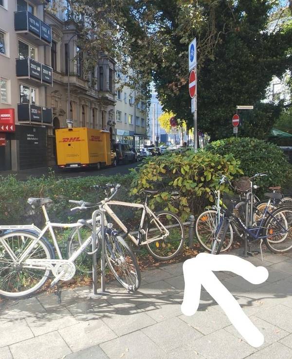 Ein Pfeil zeigt auf eine Stelle zwischen geparkten Fahrrädern.