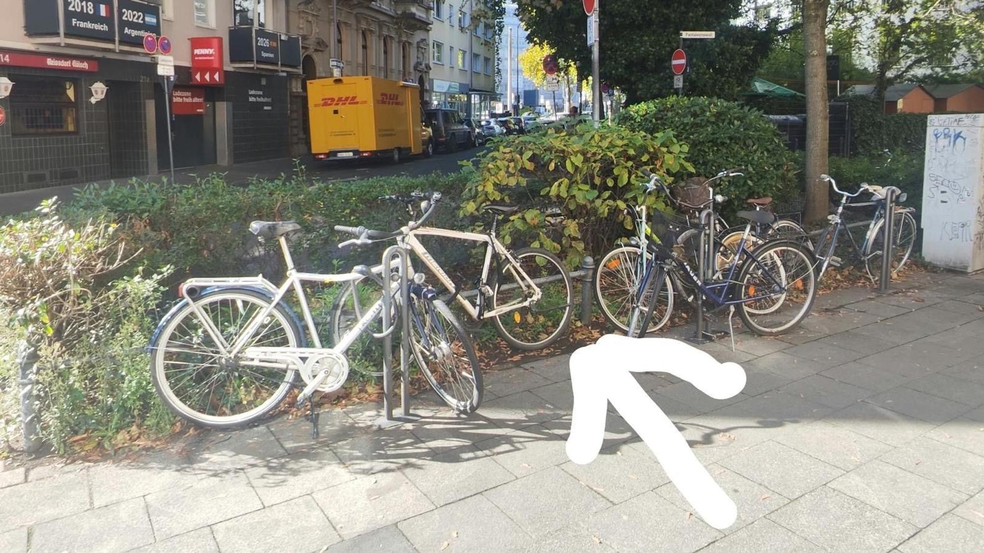 Ein Pfeil zeigt auf eine Stelle zwischen geparkten Fahrrädern.