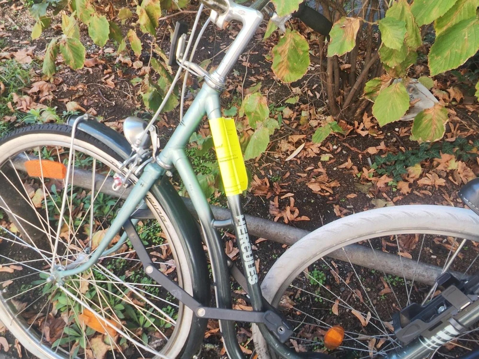 An einem abgestellten Fahrrad wurde ein knallgelber Zettel befestigt.