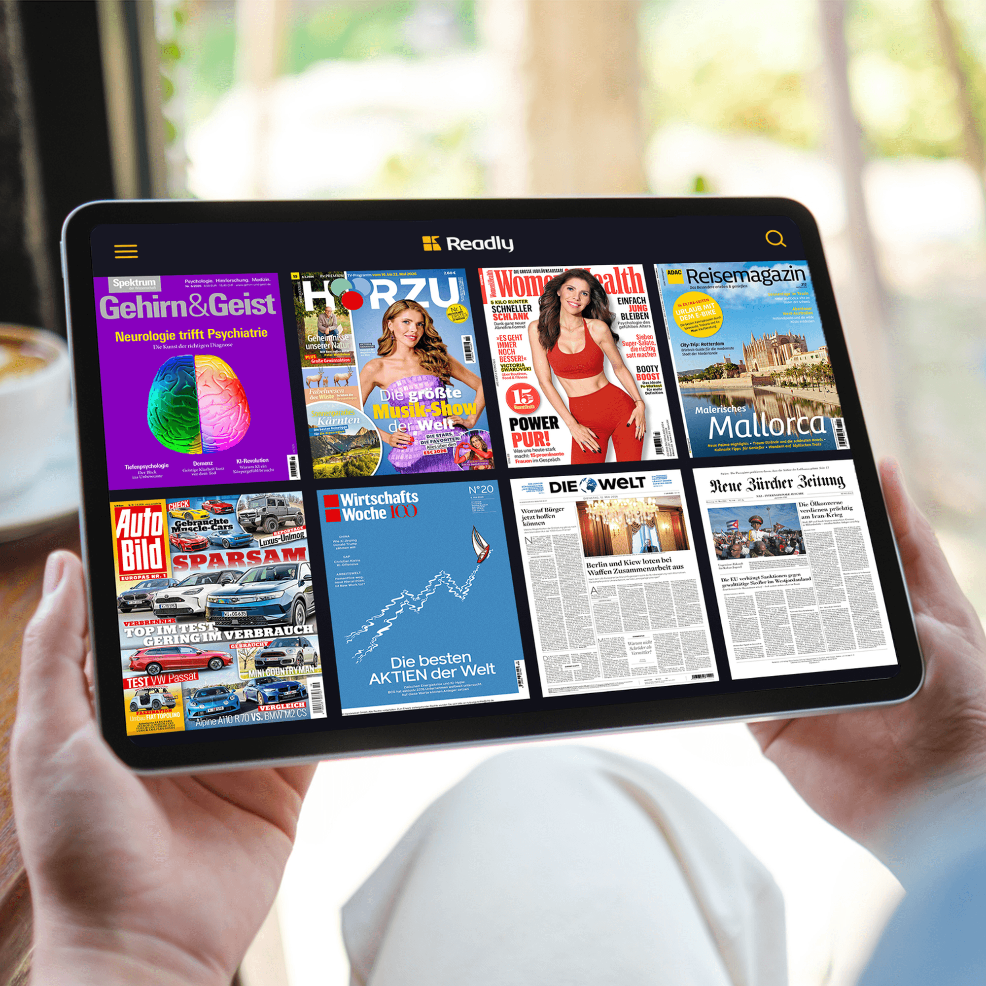 Mehrere Zeitschriftentitel in einer App auf einem Tablet-Display, gehalten von zwei Händen.