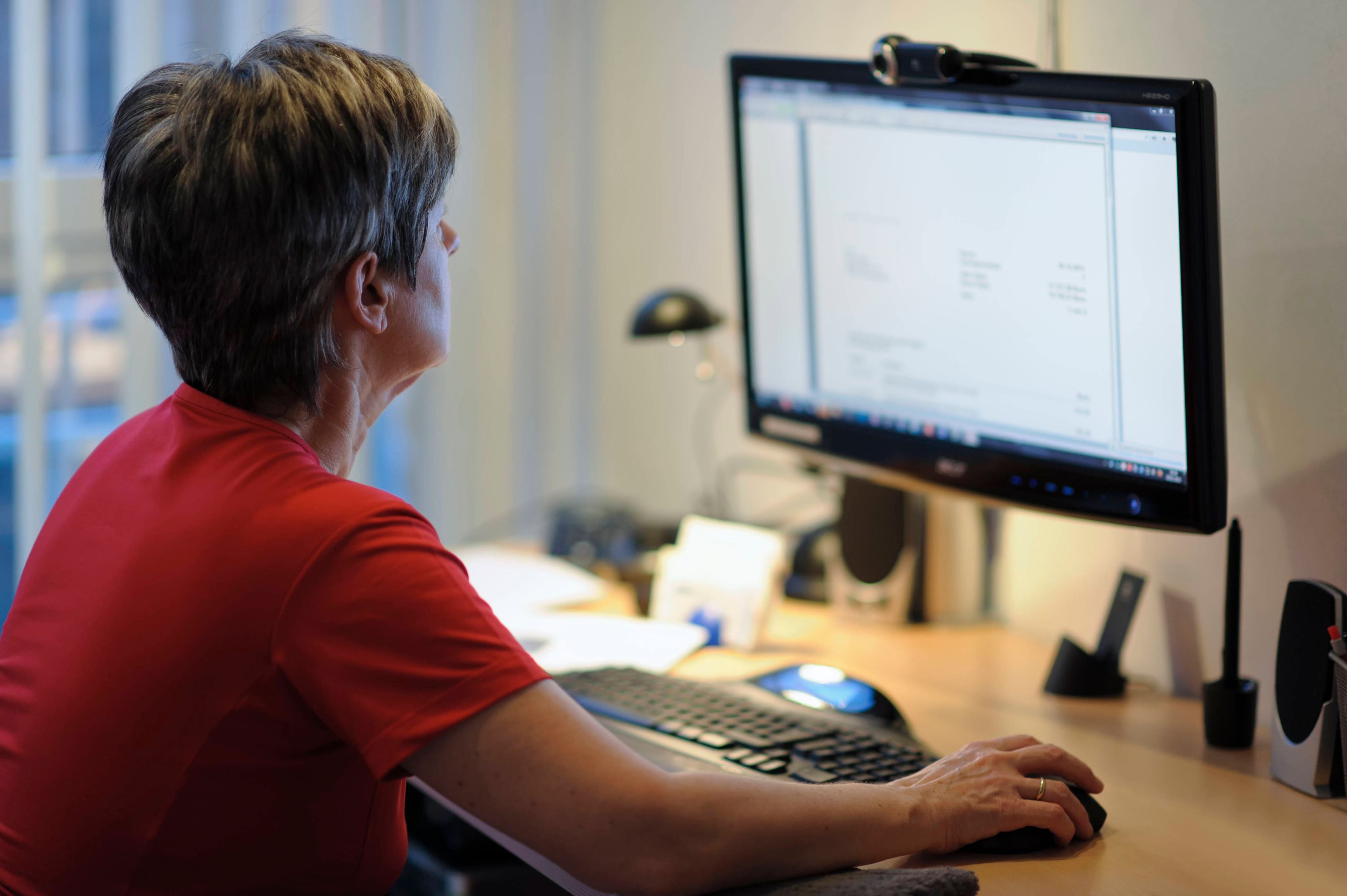 Eine Frau sitzt am Schreibtisch vor einem PC, die rechte Hand liegt auf der Maus.