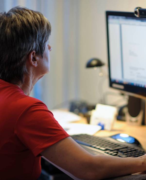 Eine Frau sitzt am Schreibtisch vor einem PC, die rechte Hand liegt auf der Maus.