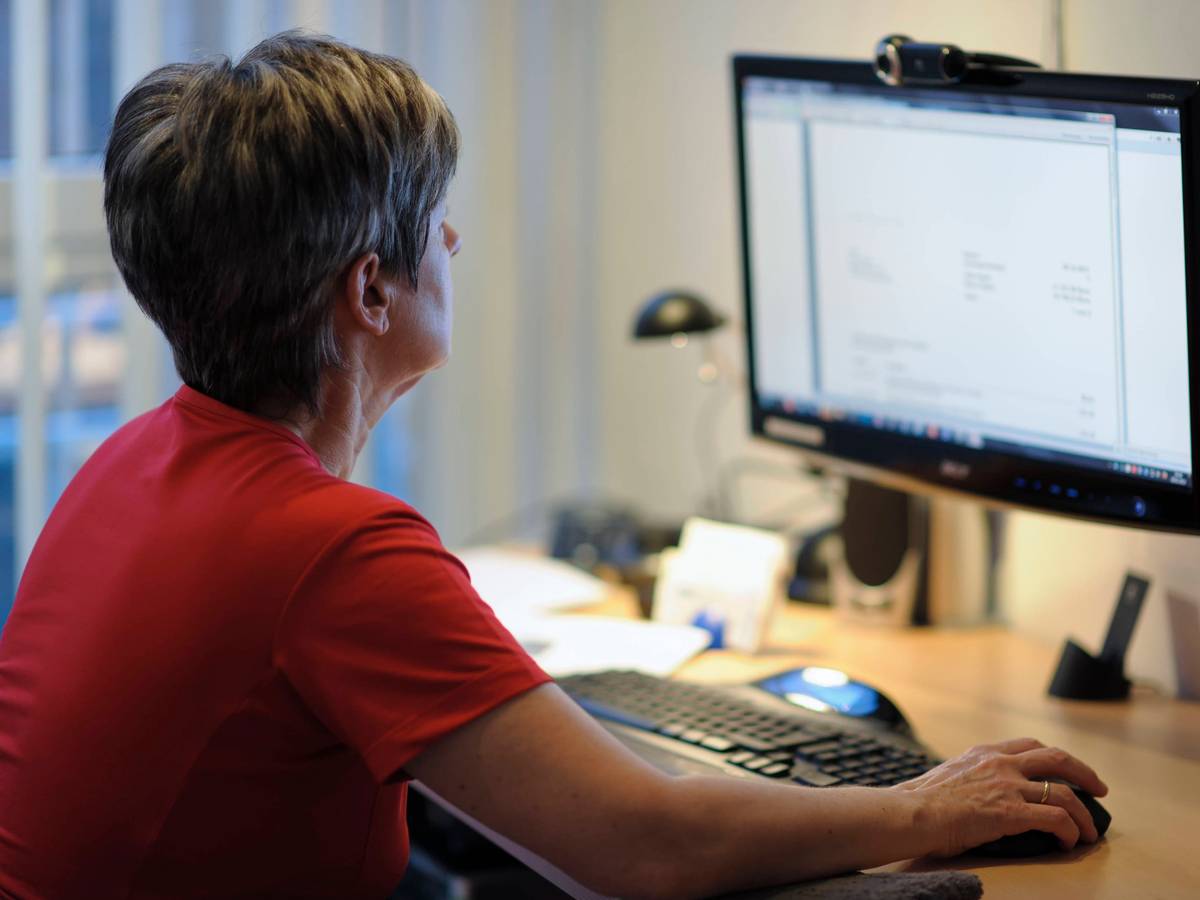 Eine Frau sitzt am Schreibtisch vor einem PC, die rechte Hand liegt auf der Maus.
