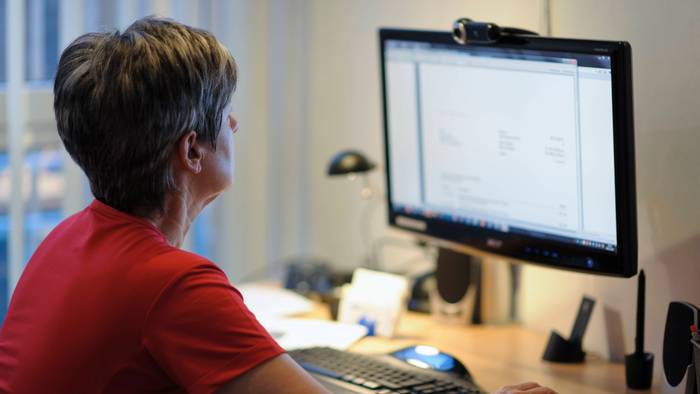 Eine Frau sitzt am Schreibtisch vor einem PC, die rechte Hand liegt auf der Maus.