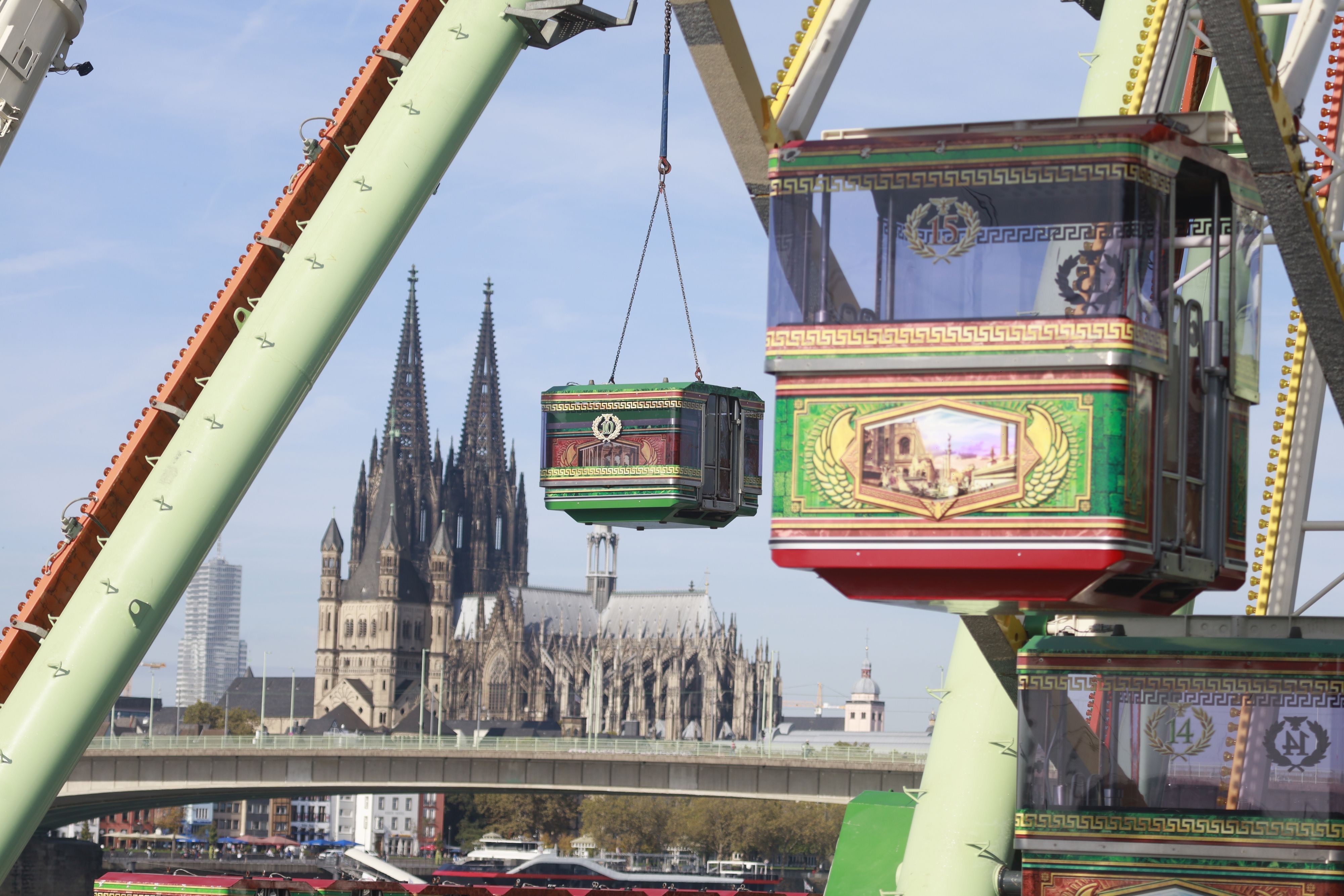 Eine Gondel des Riesenrads wird von einem Kran angehoben, im Hintergrund ist der Kölner Dom zu sehen.