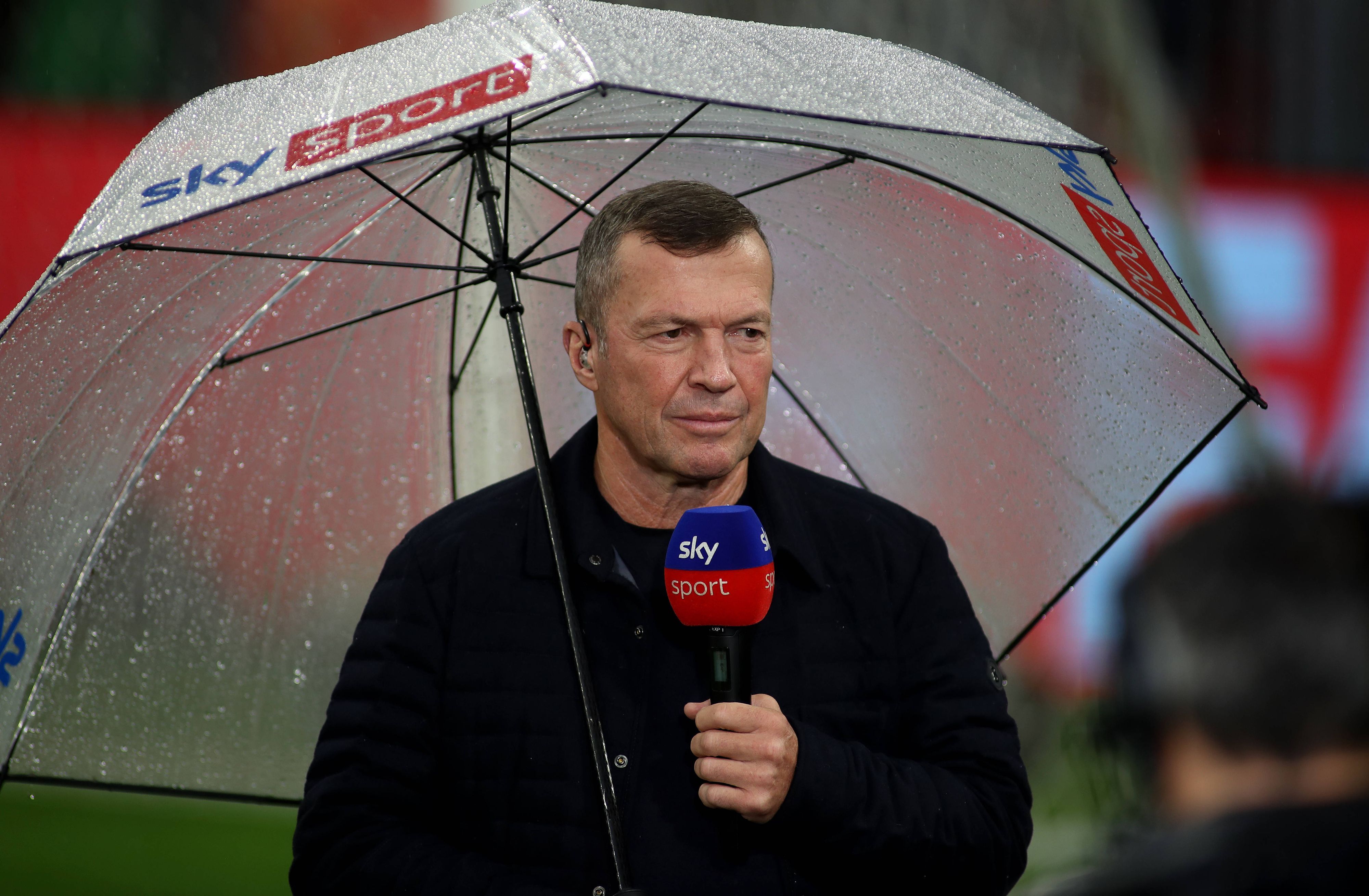 Lothar Matthäus mit Regenschirm und Sky-Mikro im Stadion.