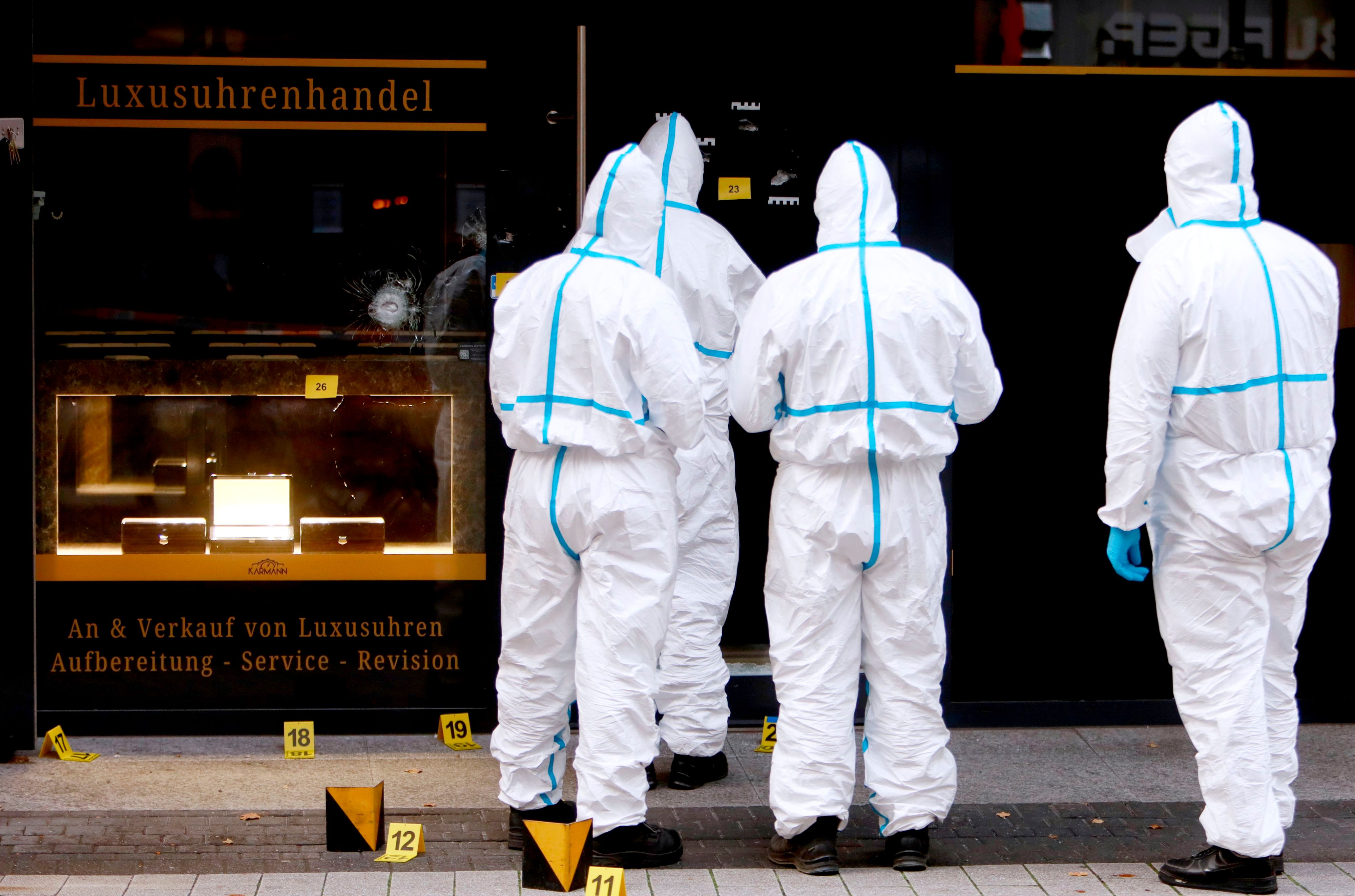 Vier Kräfte der Spurensicherung sind in Schutzanzügen vor dem Uhrengeschäft im Einsatz.