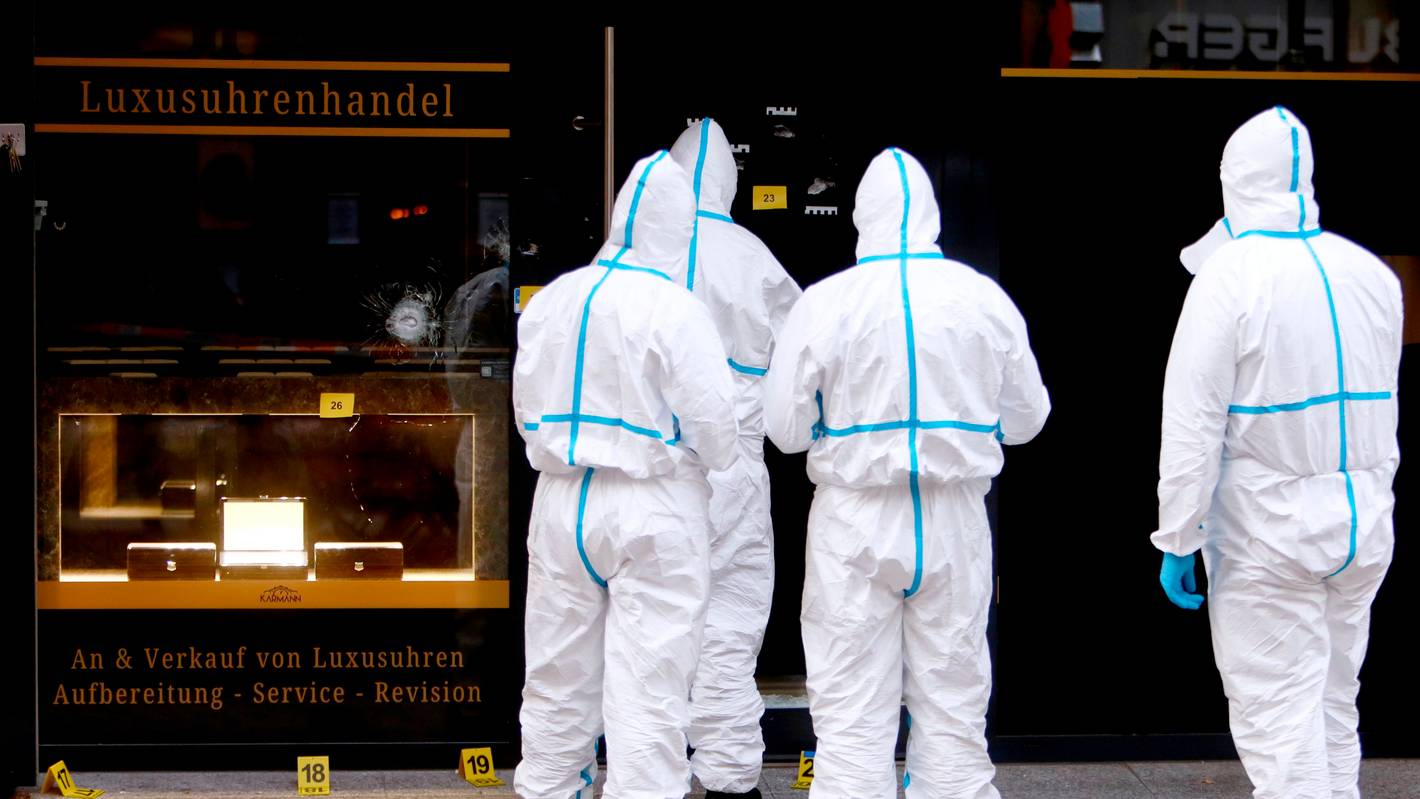 Vier Kräfte der Spurensicherung sind in Schutzanzügen vor dem Uhrengeschäft im Einsatz.