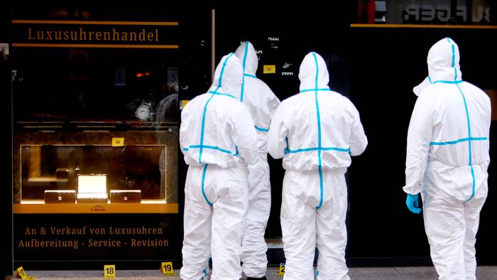 Vier Kräfte der Spurensicherung sind in Schutzanzügen vor dem Uhrengeschäft im Einsatz.