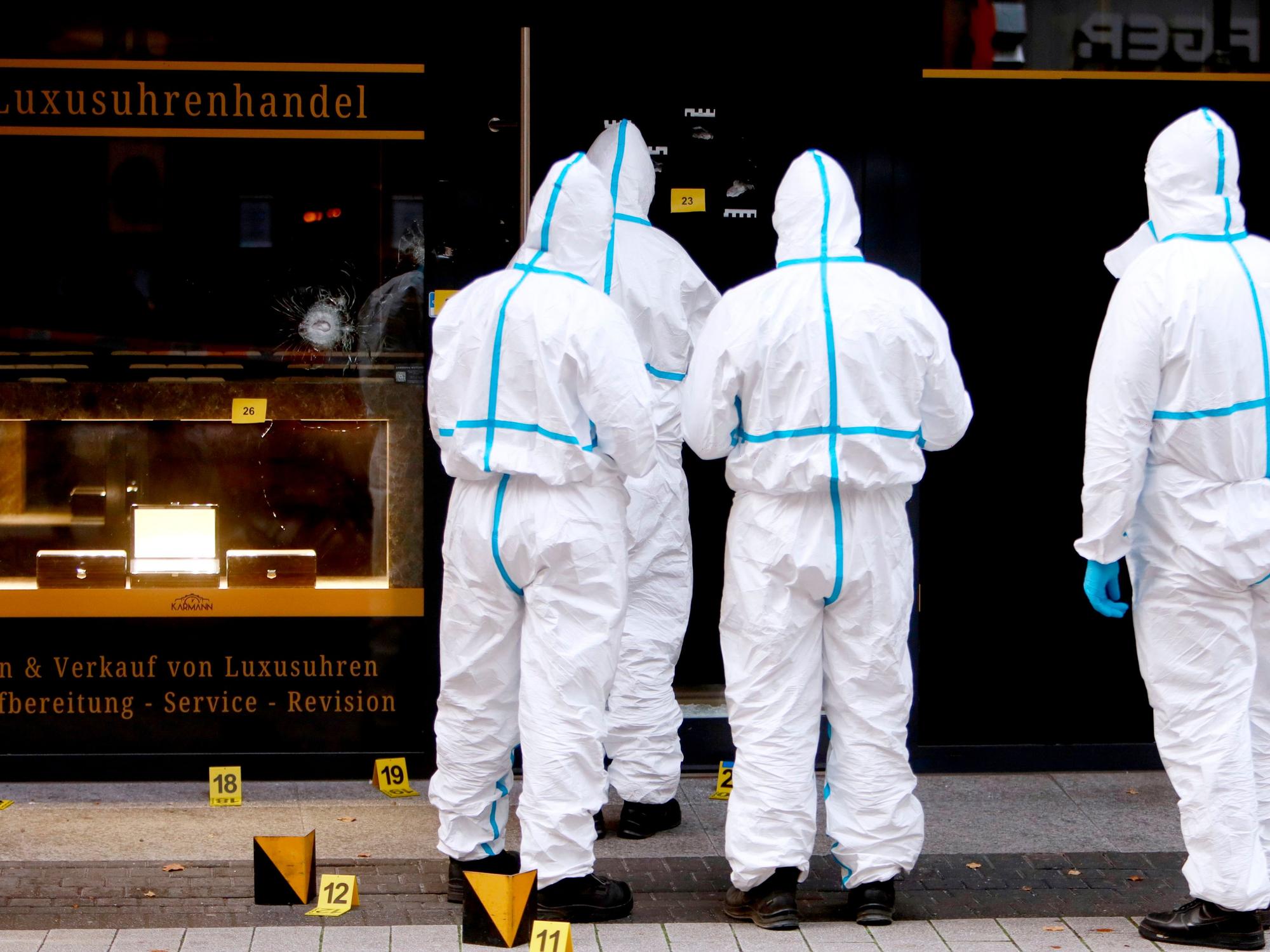 Vier Kräfte der Spurensicherung sind in Schutzanzügen vor dem Uhrengeschäft im Einsatz.