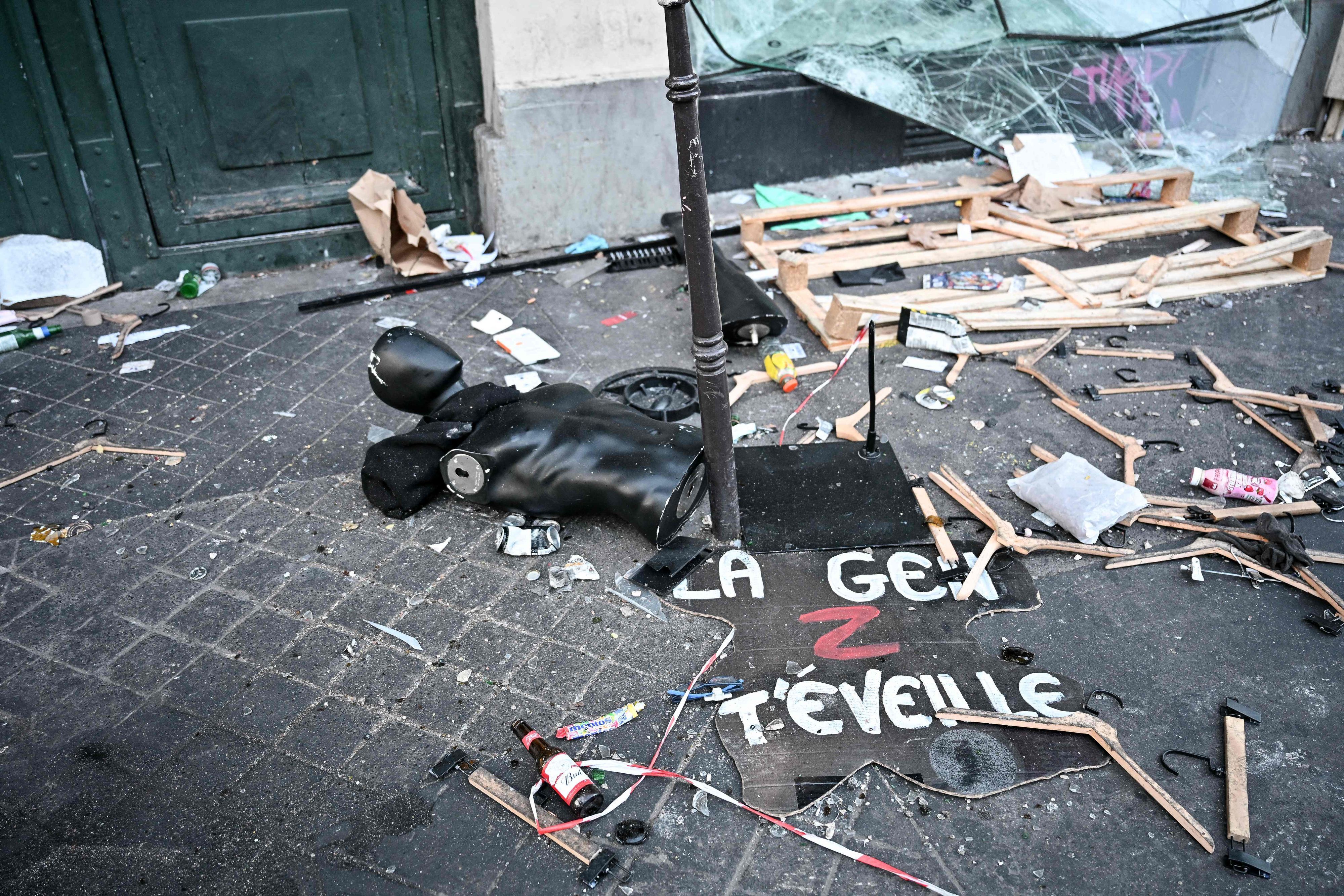 Ein Protestschild, eine zerstörte Schaufensterpuppe und Kleiderbügel liegen verstreut auf dem Boden.