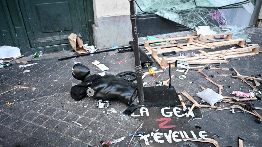 Ein Protestschild, eine zerstörte Schaufensterpuppe und Kleiderbügel liegen verstreut auf dem Boden.