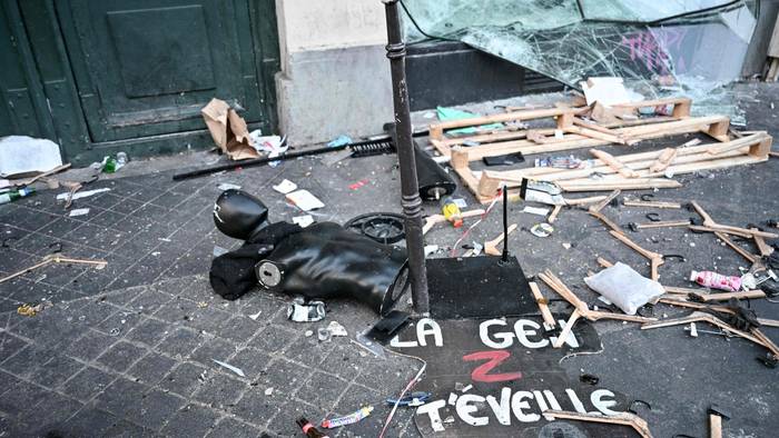 Ein Protestschild, eine zerstörte Schaufensterpuppe und Kleiderbügel liegen verstreut auf dem Boden.
