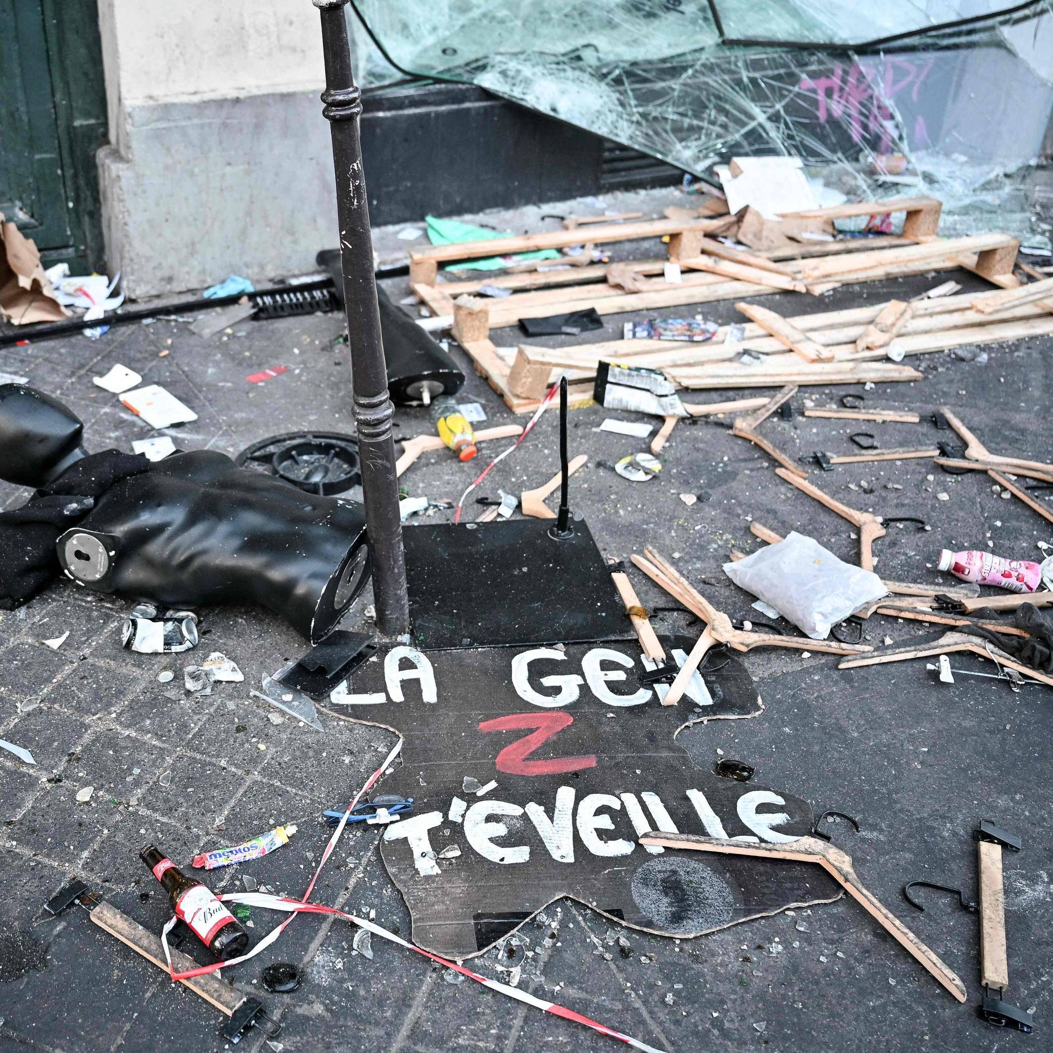 Ein Protestschild, eine zerstörte Schaufensterpuppe und Kleiderbügel liegen verstreut auf dem Boden.