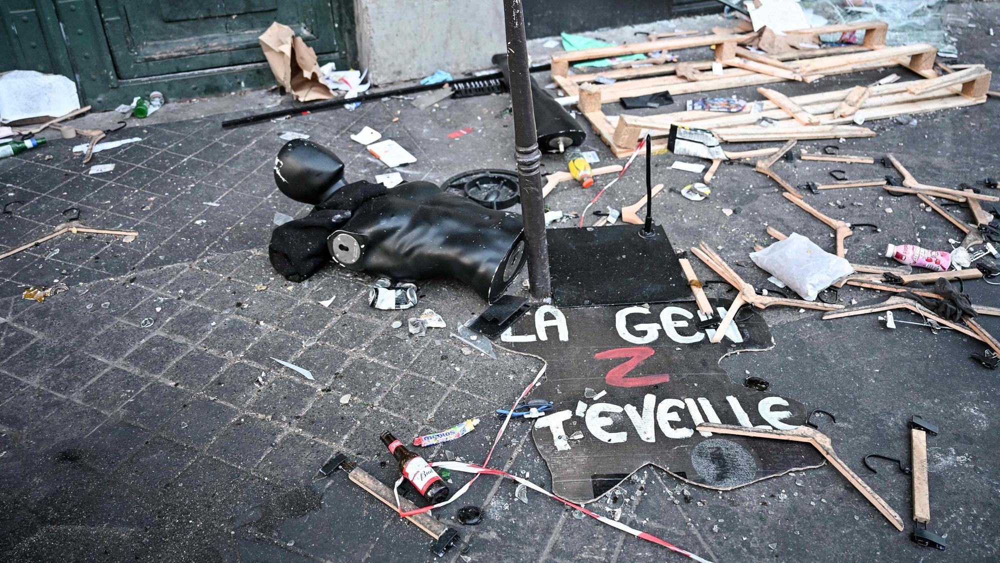 Ein Protestschild, eine zerstörte Schaufensterpuppe und Kleiderbügel liegen verstreut auf dem Boden.