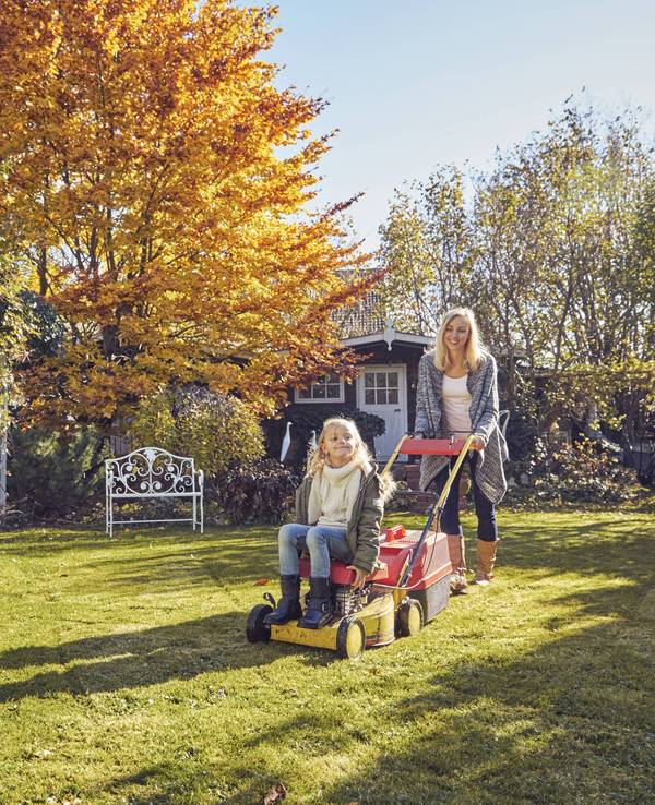 Mutter und Tochter mit einem Rasenmäher im Garten