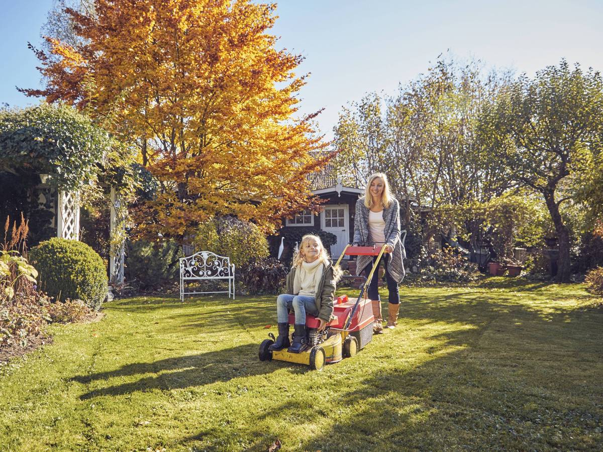 Mutter und Tochter mit einem Rasenmäher im Garten