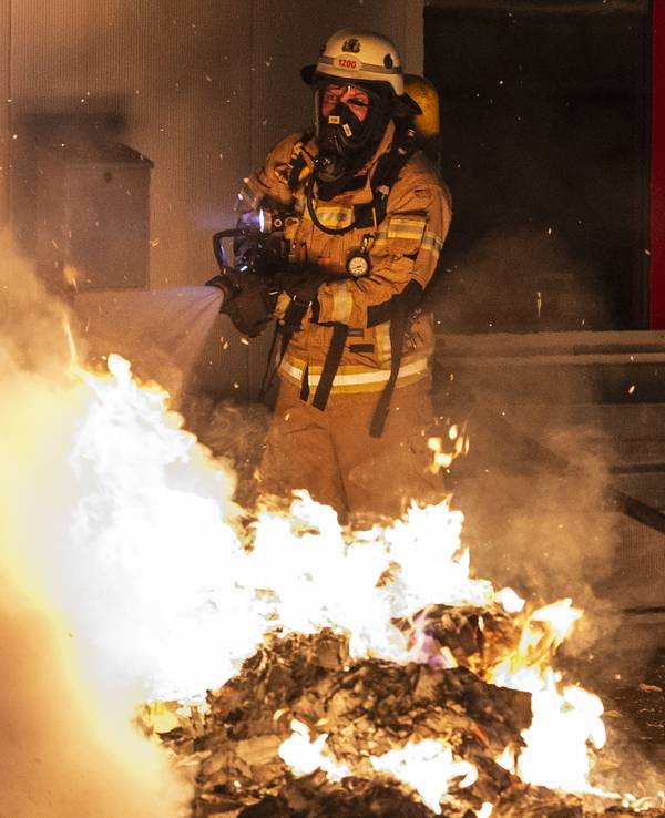 Ein Feuerwehrmann löscht eine Mülltonne.