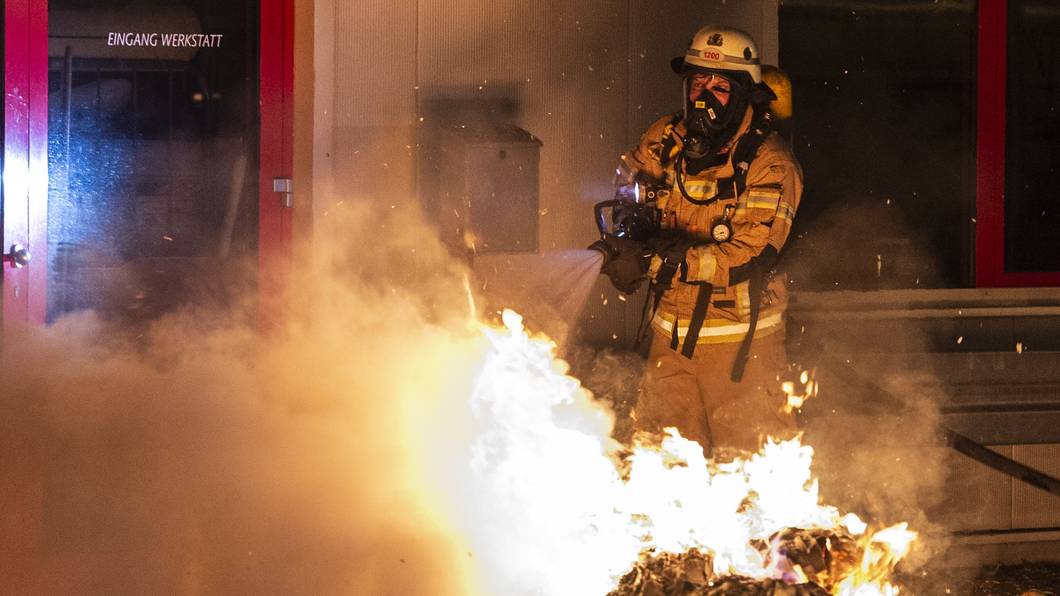 Ein Feuerwehrmann löscht eine Mülltonne.