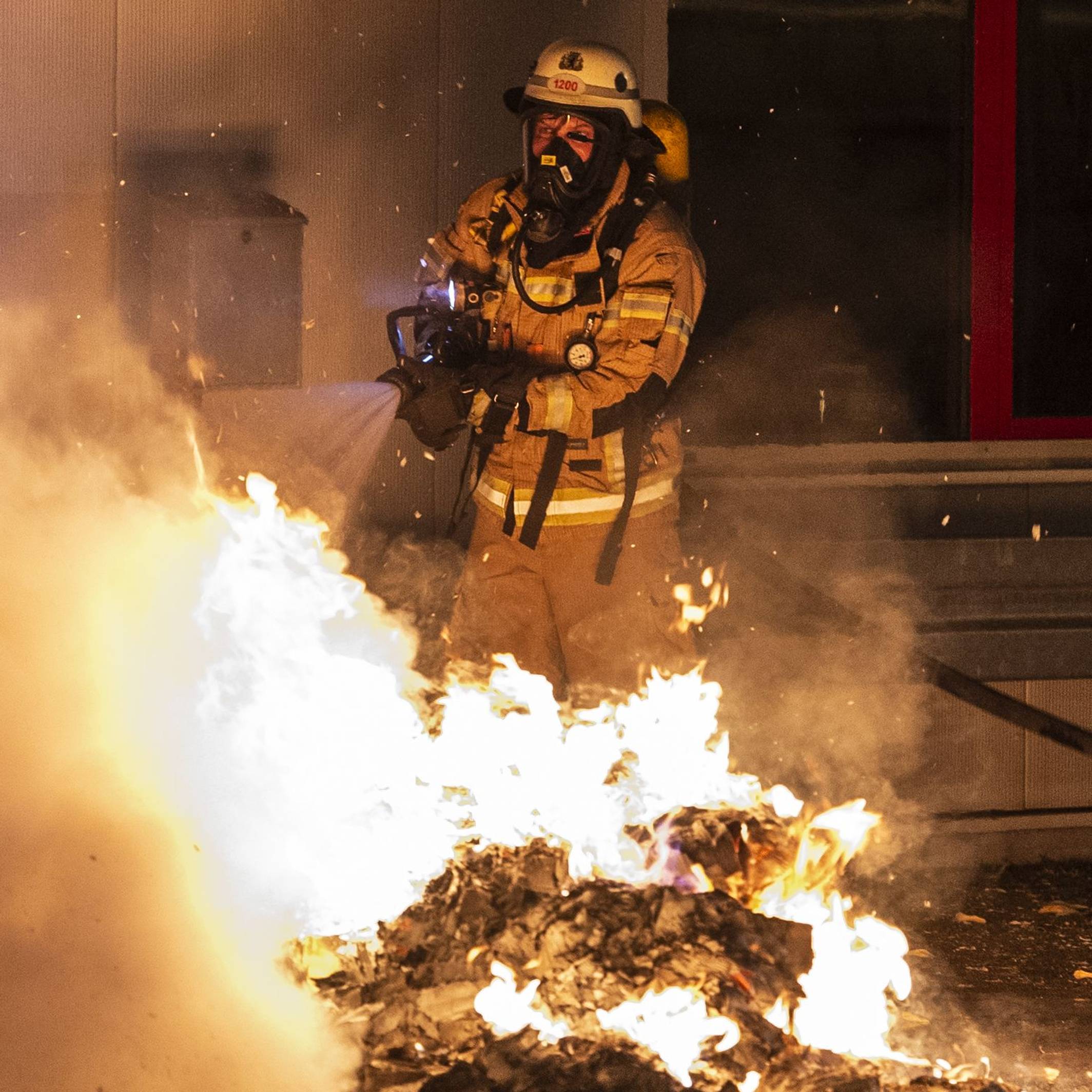 Ein Feuerwehrmann löscht eine Mülltonne.