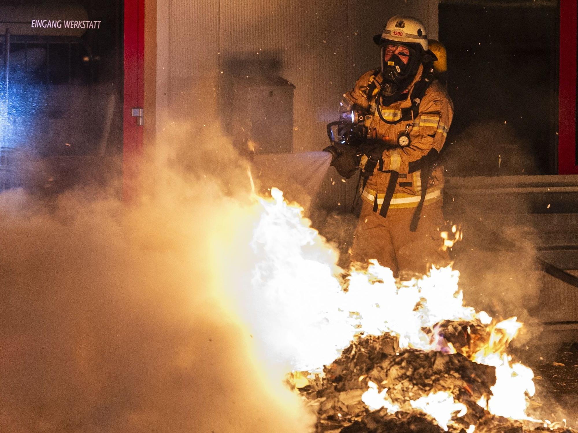 Ein Feuerwehrmann löscht eine Mülltonne.