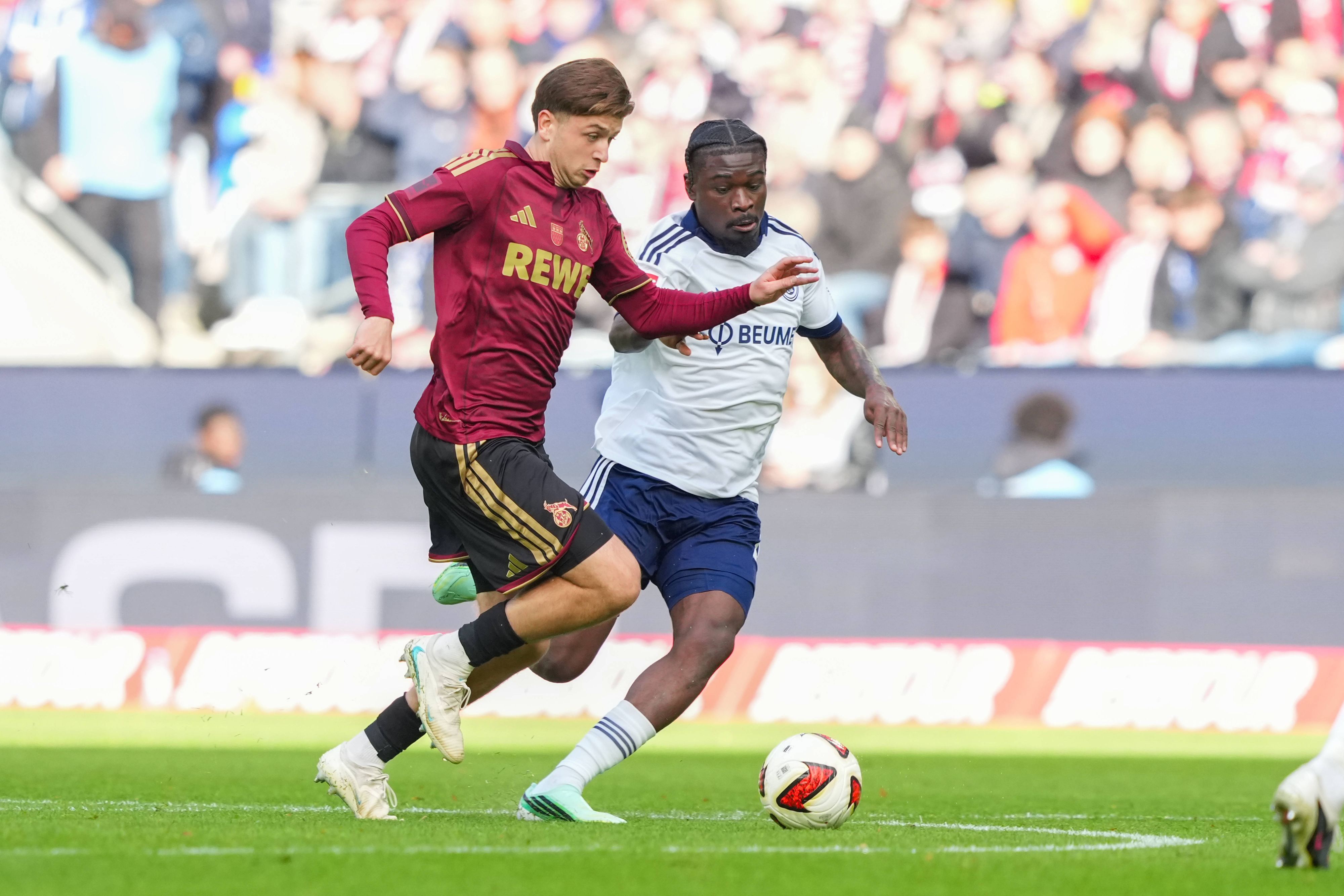 Mikey Moore (1. FC Köln)  im Zweikampf gegen Junior Dina Ebimbe (FC Schalke 04).