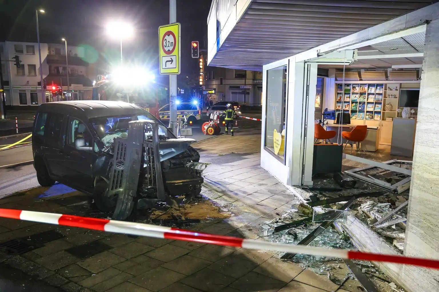 Hinter Absperrband steht ein demoliertes Auto vor einer kaputten Schaufensterscheibe. Ein Autofahrer ist am Samstagabend aus bislang ungeklärten Gründen mit seinem Wagen in ein Reisebüro gefahren.