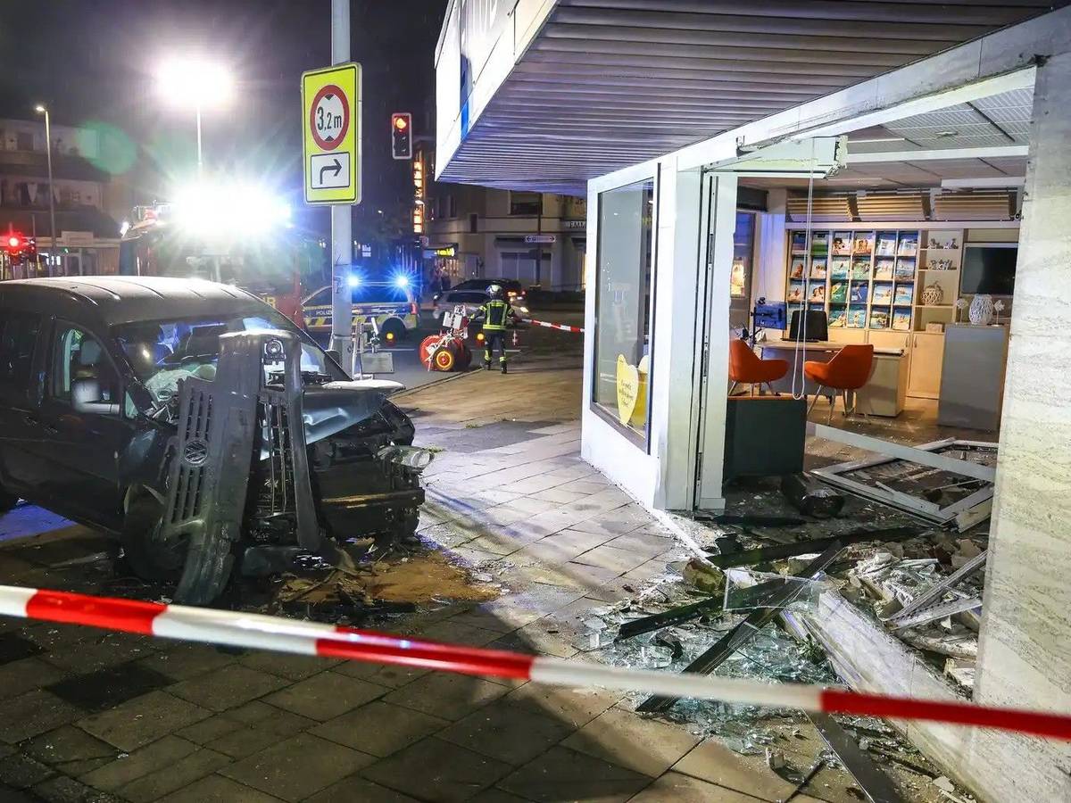 Hinter Absperrband steht ein demoliertes Auto vor einer kaputten Schaufensterscheibe. Ein Autofahrer ist am Samstagabend aus bislang ungeklärten Gründen mit seinem Wagen in ein Reisebüro gefahren.