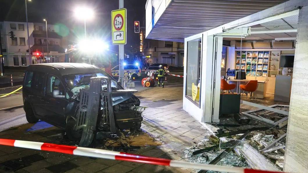 Hinter Absperrband steht ein demoliertes Auto vor einer kaputten Schaufensterscheibe. Ein Autofahrer ist am Samstagabend aus bislang ungeklärten Gründen mit seinem Wagen in ein Reisebüro gefahren.