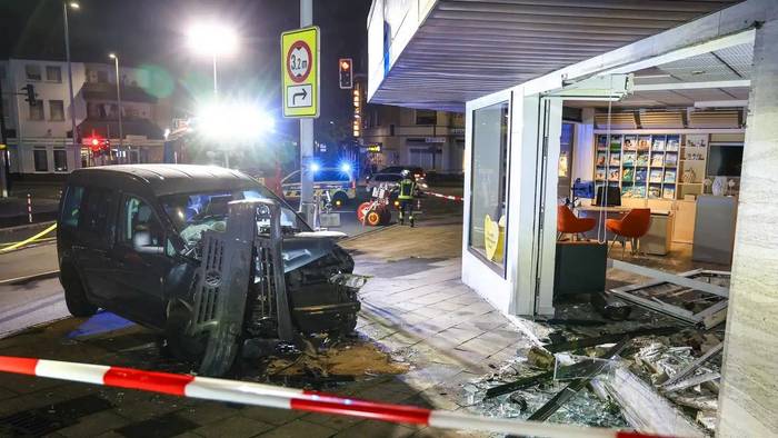 Hinter Absperrband steht ein demoliertes Auto vor einer kaputten Schaufensterscheibe. Ein Autofahrer ist am Samstagabend aus bislang ungeklärten Gründen mit seinem Wagen in ein Reisebüro gefahren.