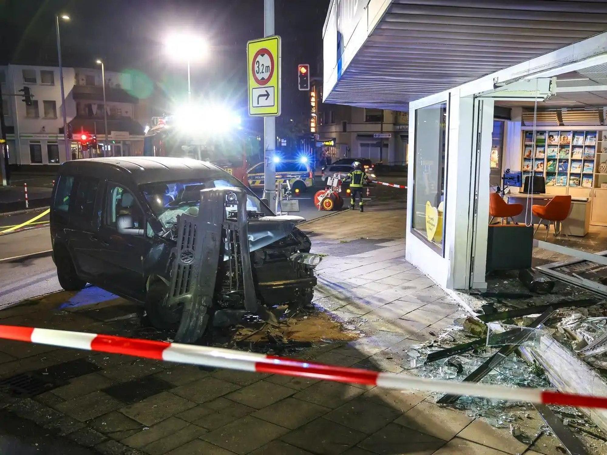 Hinter Absperrband steht ein demoliertes Auto vor einer kaputten Schaufensterscheibe. Ein Autofahrer ist am Samstagabend aus bislang ungeklärten Gründen mit seinem Wagen in ein Reisebüro gefahren.