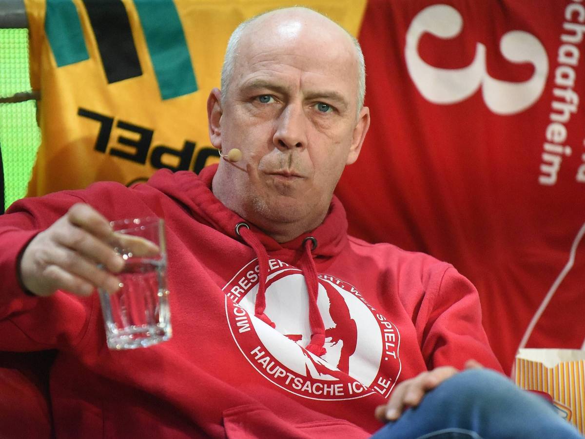 Mario Basler trinkt bei einer Veranstaltung auf der Bühne einen Schluck Wasser.