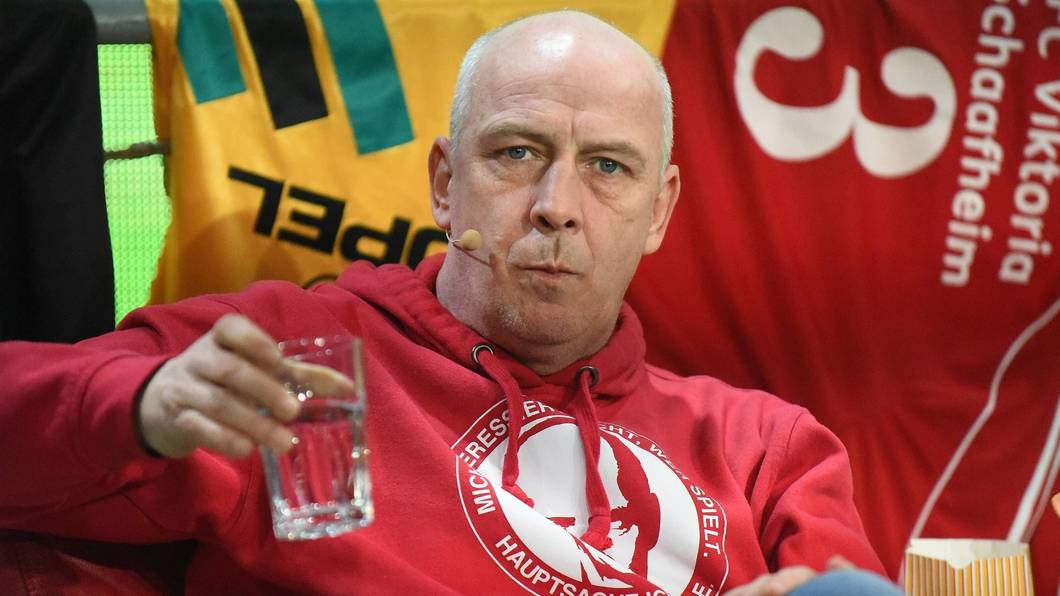Mario Basler trinkt bei einer Veranstaltung auf der Bühne einen Schluck Wasser.