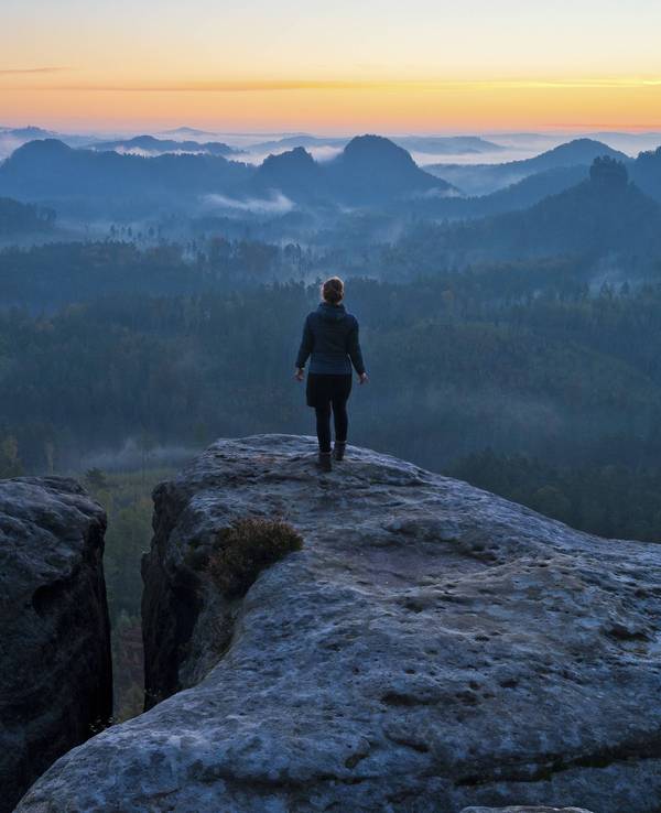 Wanderin steht bei Dämmerung auf Aussicht.